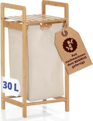 A bamboo laundry basket with a beige fabric liner, shown against a white background. A tag with German text and a bamboo graphic is attached to the side.