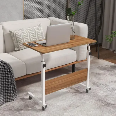 A mobile laptop table with a laptop and phone on it, placed next to a sofa in a living room.