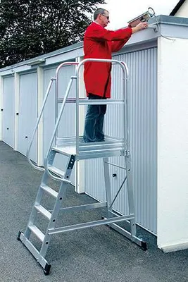 A man in a red jacket is working on a light fixture on top of a building, standing on a platform ladder.