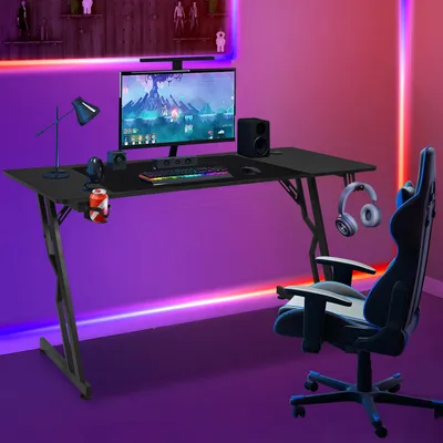 A gaming desk setup with a computer, keyboard, mouse, speakers, headphones, and a gaming chair, illuminated by colorful LED lighting.