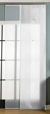 A white panel curtain with a laser-cut pattern hangs in front of a window with a grid pattern. The curtain is on a track system.