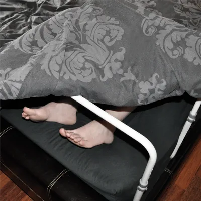Feet under a blanket with a bed frame support.