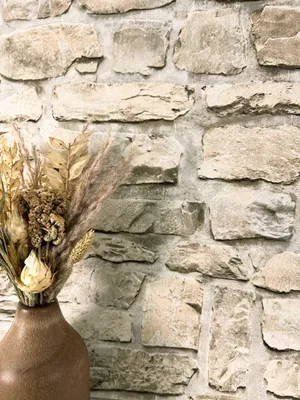 A close-up view of a vase with dried flowers in front of a stone wall.