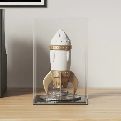 A white and gold rocket figurine displayed inside a clear acrylic case on a wooden surface.