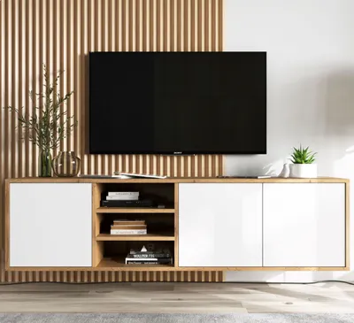 A modern TV stand with white cabinet doors and open shelving, holding books and electronics, with a large TV mounted on a slatted wooden wall.
