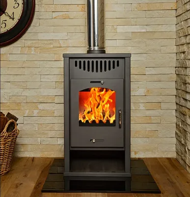 A wood-burning stove with a fire burning inside, set against a stone wall.