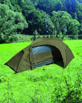 A green tent is set up on a grassy field with trees in the background.