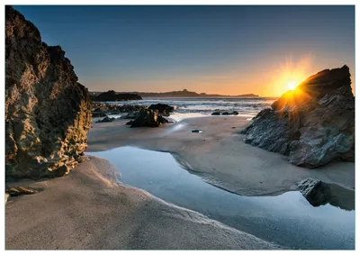 Produktbild von Wallario Premium Glasbild, freischwebende Optik, kräftige Farben, Größe 100 x 70 cm Motiv Sonnenuntergang hinter einem Felsen am Strand