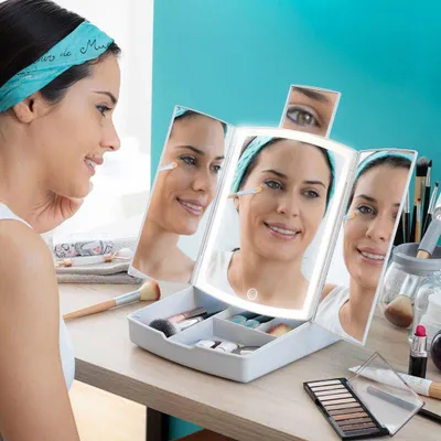 A woman is applying makeup using a lighted makeup mirror with storage compartments.