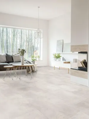 A modern living room with a large window overlooking a forest, featuring a sofa, coffee table, and fireplace.
