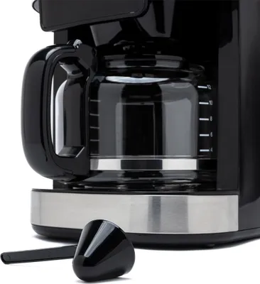 Close-up of a black coffee maker with a glass carafe and a silver base. A black scoop is in the foreground.