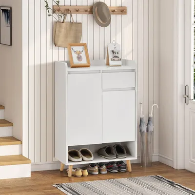 A white shoe cabinet with wooden legs is shown in a hallway setting, with stairs to the left and a door to the right.