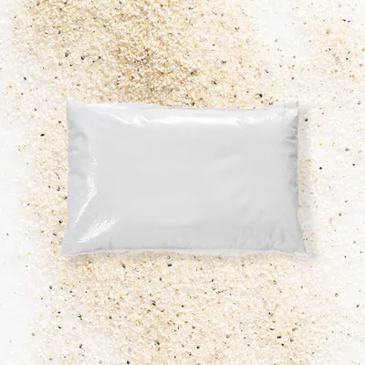 A white bag of sand is placed on a surface covered with sand.