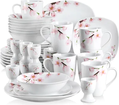 A collection of white ceramic dinnerware with a pink cherry blossom pattern, arranged in a studio setting.