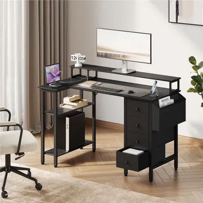 A black L-shaped computer desk with a monitor, laptop, keyboard, and drawers, set up in a home office environment.