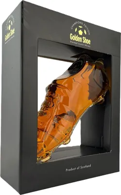 A bottle of Golden Shoe whisky shaped like a soccer cleat, presented in its retail packaging.