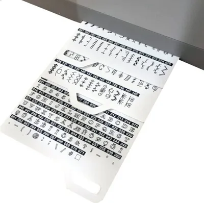 A close-up view of a perforated card with lines of stitch patterns and alphanumeric characters, likely for a sewing machine, emerging from a machine.