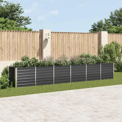 A raised garden bed filled with plants is situated in a garden setting with a wooden fence and paved patio.