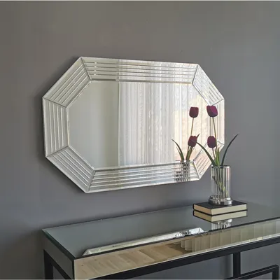 A decorative mirror is mounted on a gray wall above a console table. Two vases with artificial flowers are placed on the table.