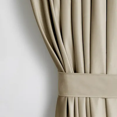 A close-up view of a beige velvet curtain with pleats and a tie-back.