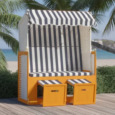 A beach chair with a striped canopy sits on a wooden deck near a beach with palm trees.