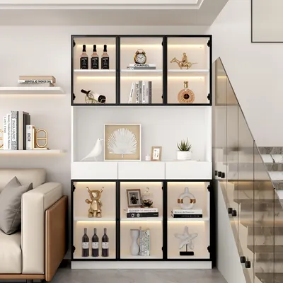 A modern living room with a display cabinet filled with decorative items and bottles, next to a sofa and a staircase.