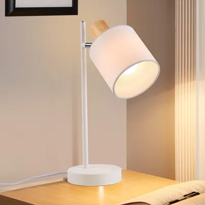 A white desk lamp with a fabric shade and wooden accent sits on a wooden desk.