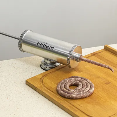 A sausage stuffer with a coiled sausage on a wooden cutting board.