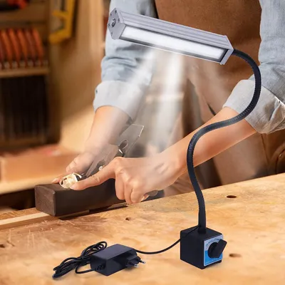 A person is using a woodworking tool under the light of a flexible LED lamp.