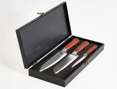 A set of three knives with wooden handles are displayed in an open black wooden box.