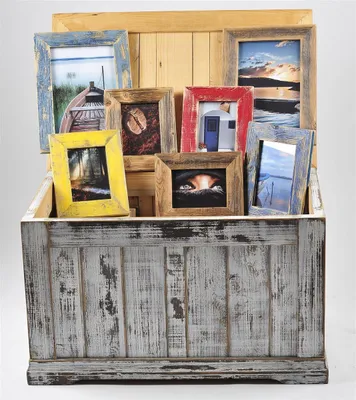 A collection of vintage-style picture frames of various colors and sizes are displayed inside a distressed wooden chest.