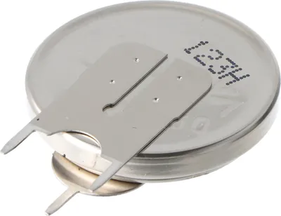 A close-up, angled view of a silver coin-cell battery with two metal tabs attached to its top surface.
