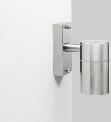 A close-up shot of a modern, cylindrical wall light fixture made of brushed metal, mounted on a white wall.