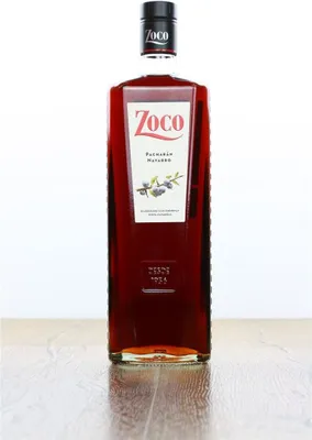 A bottle of Zoco Pacharan liqueur stands on a wooden surface against a white background.