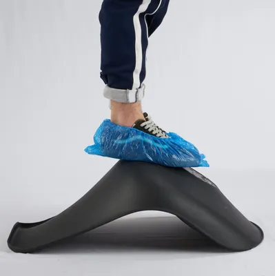 A person's leg and foot wearing a blue disposable shoe cover is shown standing on a black object.