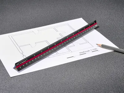 A triangular ruler is placed on a blueprint with a pencil nearby.