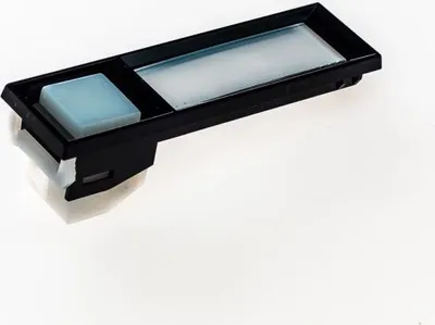 A close-up studio shot of a black electronic component with a light blue button and a translucent rectangular display area, set against a white background.