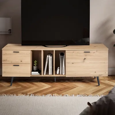 A modern wooden TV stand with drawers and shelves, holding books and a game console, in a living room setting.