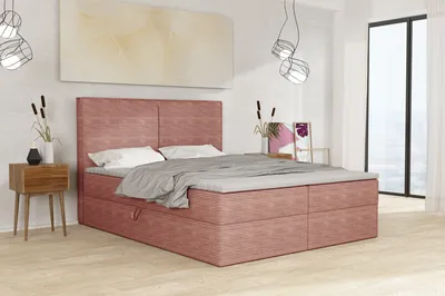 A bedroom scene featuring a pink upholstered bed with a topper, a wooden nightstand, and decorative items.