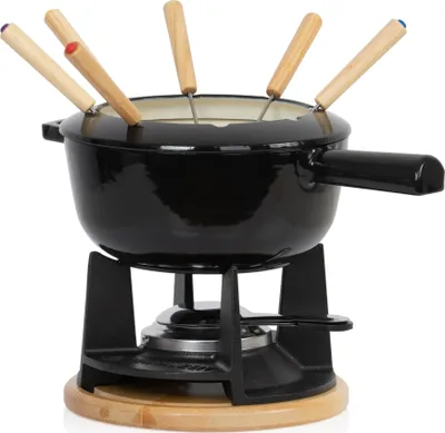 A black cast iron fondue set with wooden-handled fondue forks sits on a wooden base above a burner.