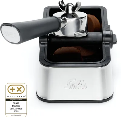 A coffee portafilter is placed in a knock box, with coffee grounds visible inside the box.