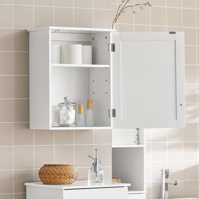 A white bathroom cabinet with its door open, showing shelves with items like toilet paper rolls and bottles. The cabinet is mounted on a tiled wall.