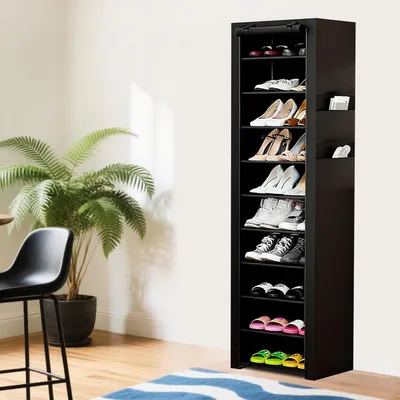A tall, black shoe rack filled with various shoes is shown in a room with a plant and a chair.