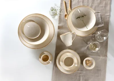 A collection of ceramic tableware, including plates, bowls, and cups, arranged on a neutral-colored runner.