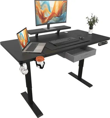 A black electric standing desk with a laptop, monitor, keyboard, and a drawer. There is also a cup holder with a cup and headphones attached to the side.
