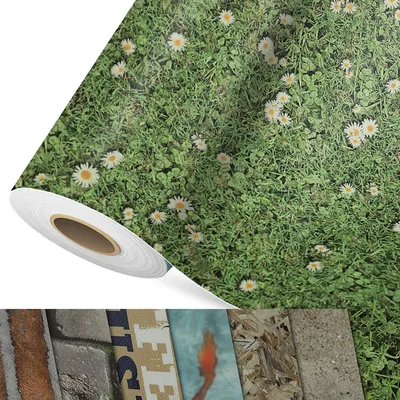 A roll of flooring with a daisy meadow print is shown diagonally across the image, with a white roll in the foreground and a green, grassy meadow with daisies filling the rest of the frame. Below the roll, a strip of different flooring materials is visible