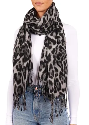 A woman wearing a white long-sleeved shirt and blue jeans is modeling a leopard-print scarf.