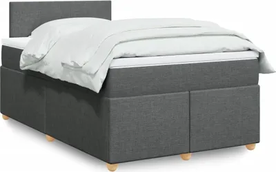 A dark gray upholstered box spring bed with a white duvet and pillows, shown from a side angle.