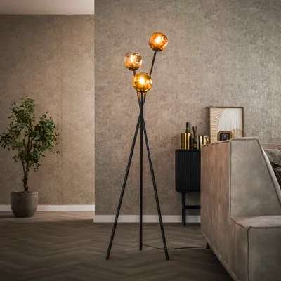 A modern living room with a tripod floor lamp with three amber glass globes, a potted plant, and a sofa.
