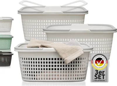 A set of three white laundry baskets with gray lids and handles, stacked and arranged on a white background. Smaller baskets in green and brown are visible on the left.
